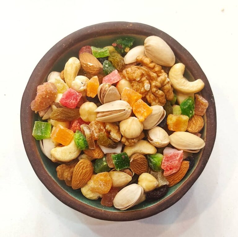 یک کاسه سرامیکی پر از آجیل استوایی که مخلوطی از بادام هندی پسته گردو کشمش مویز و جیه میوه استوایی است