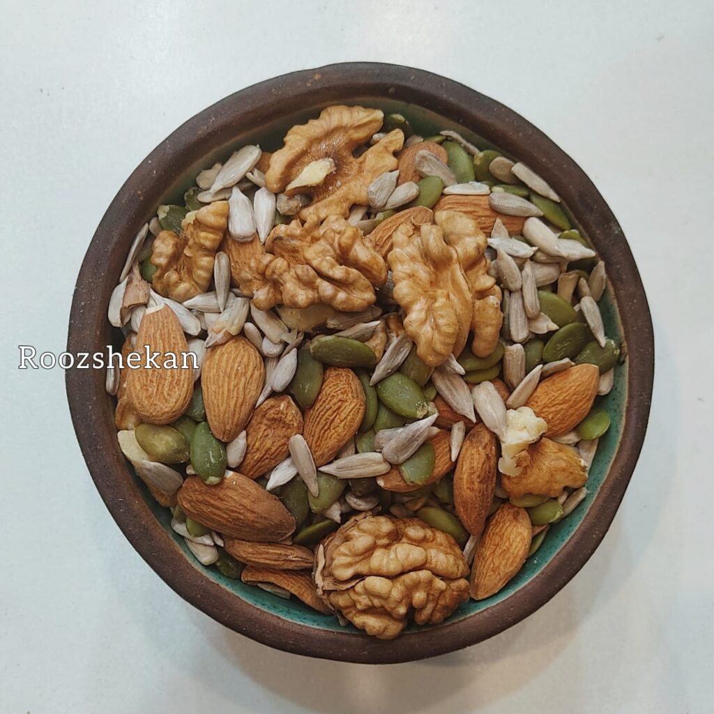 یک کاسه سرامیکی پر از آجیل کتوژنیک که ترکیبی از مغز گردو مغز بادام درختی مغز کدو و مغز آفتابگردان